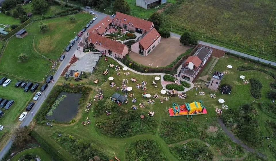 Luchtfoto van een familiefeest op het domein, met springkasteel, parasols en de vijver